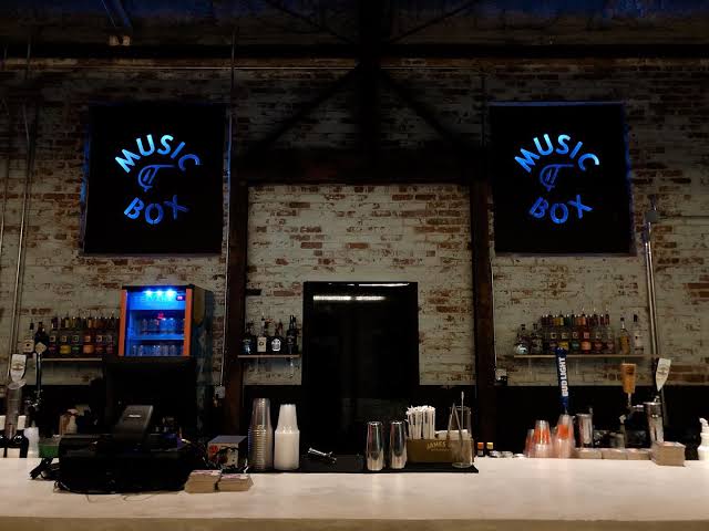 The wall-to-wall bar inside the Music Box, lit by twin neon Music Box signs on exposed brick.